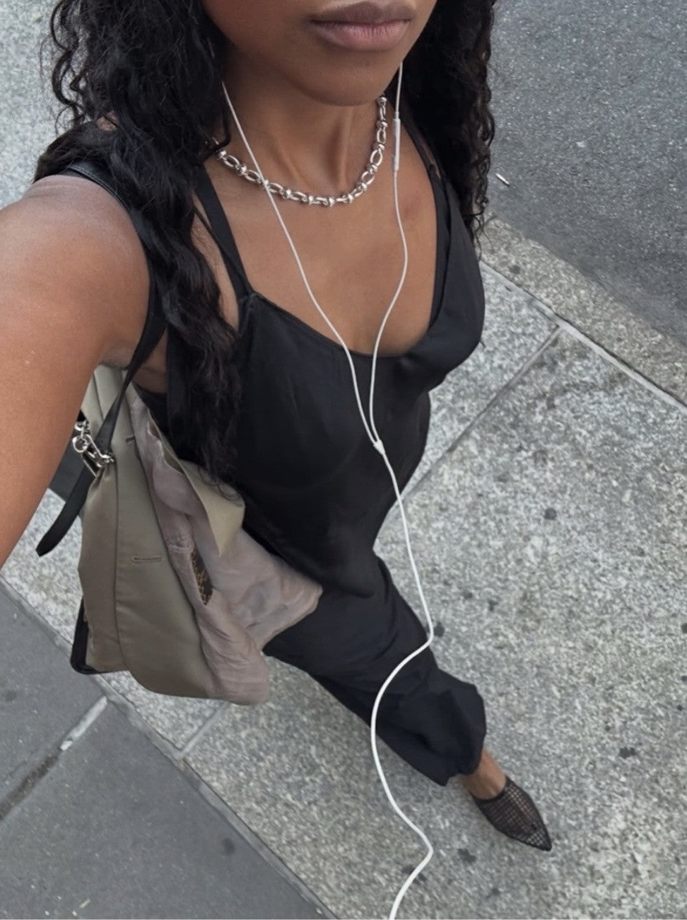 Maya wearing Hollow necklace, a black sleeveless top and black pants on a sidewalk.