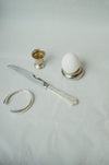 Silver knife and egg holder with a white egg on a light gray background