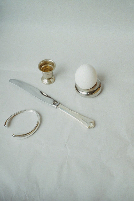 Silver knife and egg holder with a white egg on a light gray background